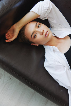Women lying at home on the couch portrait with a short haircut in a white shirt, smile, depression...
