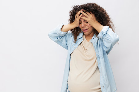 Pregnant woman tired, headache tears and frustration, difficult pregnancy, the last month before childbirth on a white isolated background in a T-shirt with a blue shirtの写真素材