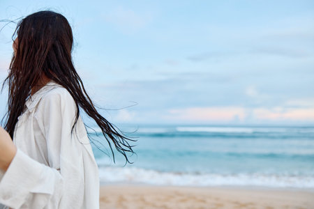 Brunette woman with long hair in a white shirt and denim shorts smile and happiness running on the beach and having fun smile with teeth in front of the ocean, vacation summer tripの写真素材