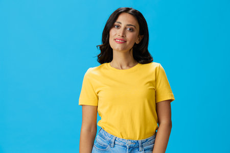 Woman in yellow t-shirt on blue background posing gestures emotions and signals with smile, hands up...