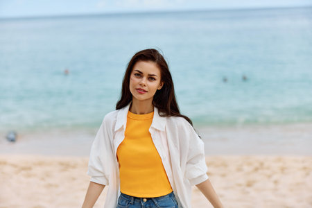 Happy woman smile with teeth with long hair brunette walks along the beach in a yellow t-shirt denim...