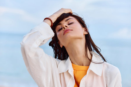 Portrait of a beautiful pensive woman with tanned skin in a yellow tank top and white beach shirt with wet hair after swimming on the ocean beach sunset lightの写真素材