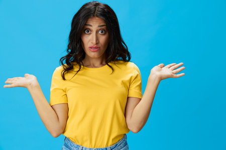 Woman in yellow t-shirt on blue background posing gestures emotions and signals with smile, hands up happiness copy spaceの写真素材