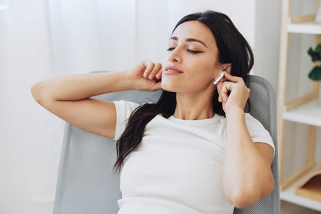 Woman listening to music on headphones sitting at home on a chair with her eyes closed, a smile and a good mood, a meditation to relieve stressの写真素材