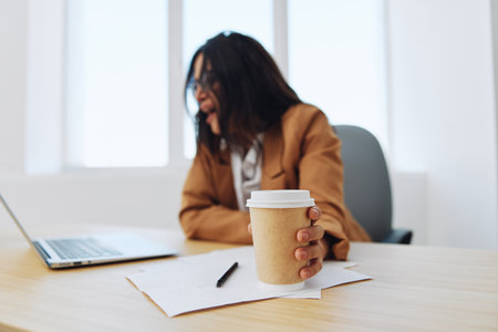 Woman business works in the office at the desk in the office in a beige suit, glasses with a cup of coffee, autumn mood, tiredness coffee breakの写真素材