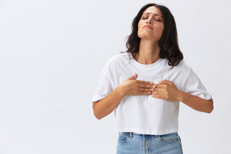 Woman ling pain heart pain, pre-stroke condition, spasm in the chest area at a young age, a woman in a white t-shirt and jeans on a white background, copy spaceの写真素材