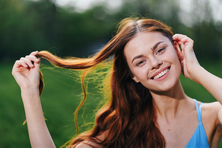 A woman in the spring nature smile with teeth touching hand long natural hair and happy, the concept of a healthy body and healthy hair in the spring and summer in the sunの写真素材