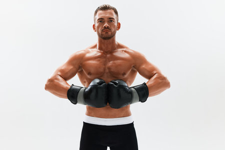 Man athletic bodybuilder poses in boxing gloves with nude torso abs in full-length background, boxing and martial arts. Advertising, sports, active lifestyle, competition, challenge concept.の写真素材