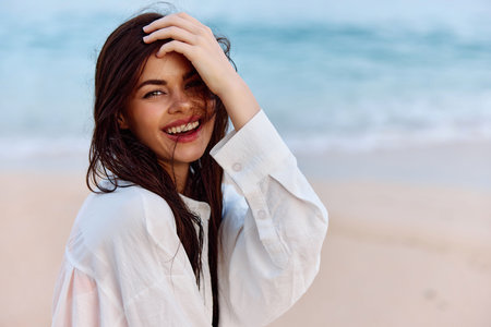 Portrait of a woman smile with teeth with tanned skin in a yellow tank top and white beach shirt with wet hair after swimming on the ocean beach sunset lightの写真素材