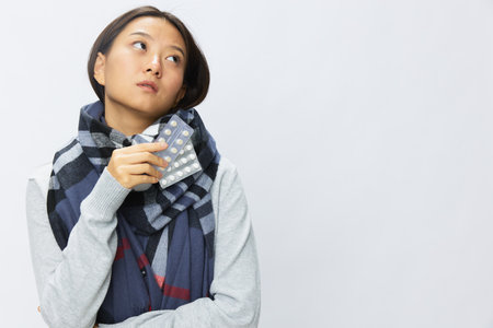 Asian woman headache cold flu holding medicine and pills in checkered plaid with fever sick of virus on white background, copy spaceの写真素材
