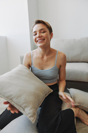 Teenage girl smile everyone sits at home near the couch and tosses up pillows, fun game and...