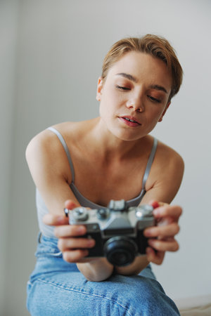 Woman photographer shooting in studio on old film camera at home on couch portrait, white...