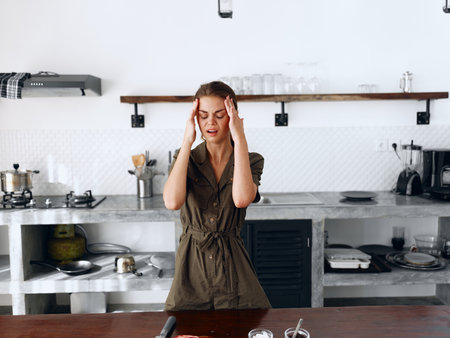 Portrait of a sad tired woman with a sore head in the kitchen, domestic problems, unstable emotional state, tears from onions, cooking dinner in the kitchen at homeの写真素材