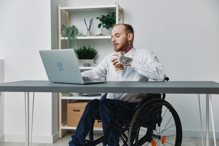 A man in a wheelchair a businessman with tattoos in the office works at a laptop with coffee, integration into society, the concept of working a person with disabilities, freedom from social frameworkの写真素材