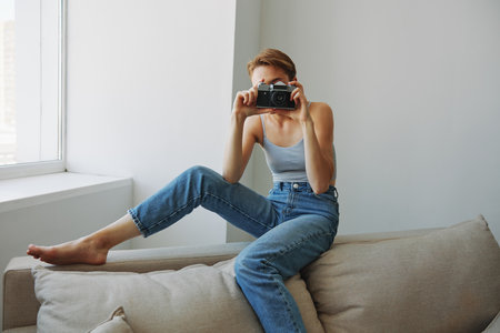 Woman photographer shooting in studio on old film camera at home on couch portrait, white background, free copy space, freelance photographerの写真素材