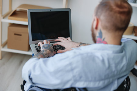 A man in a wheelchair freelancer works at a laptop at home view from the back, copy space, integration into society, health concept man with disabilities, real personの写真素材