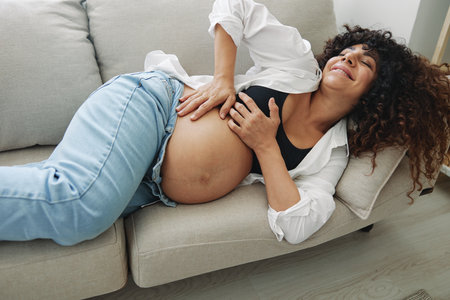 Pregnant woman smile and happiness lies on the couch freedom and strokes her belly feels kicks with the baby in the last month of pregnancy, mothers day lifestyleの写真素材