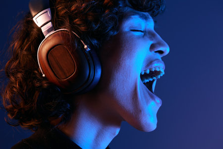 Man wearing headphones listening to music and singing with his mouth open, hipster lifestyle blogger, portrait purple background, mixed neon light, fashion style and trends, copy spaceの写真素材