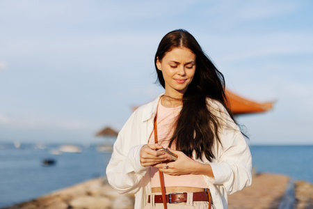 Woman smile blogger freelancer with phone in hand on vacation walking on the beach by the ocean in...