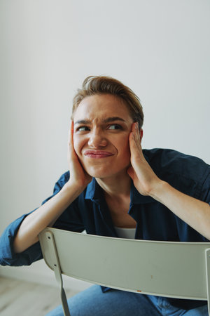 A young woman sitting in a chair at home smiling with teeth with a short haircut in jeans and a...