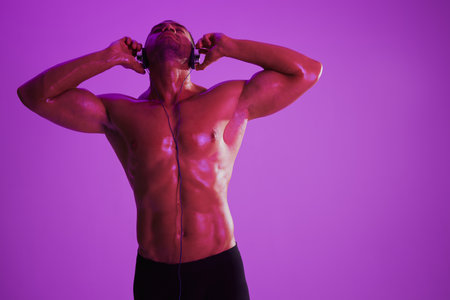 Man wearing headphones athletic physique bodybuilder nude torso abs full-length, fitness classes, purple colored light. Advertising, sports, active lifestyle, competition, challenge concept.の写真素材