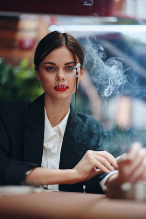 Stylish woman sits in a cafe at a table and smokes a cigarette, a bad habitの写真素材