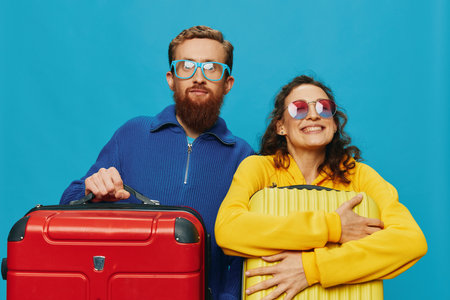 Woman and man smile suitcases in hand with yellow and red suitcase smile fun, on blue background, packing for a trip, family vacation trip.の写真素材