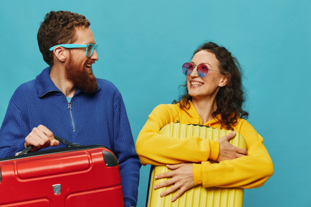 Woman and man smile suitcases in hand with yellow and red suitcase smile fun, on blue background, packing for a trip, family vacation trip.の写真素材
