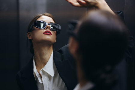 Stylish woman in a black jacket and sunglasses posing in an elevator lift near the mirror, fashion model, dark cinematic light and color matrix, glamor vintageの写真素材