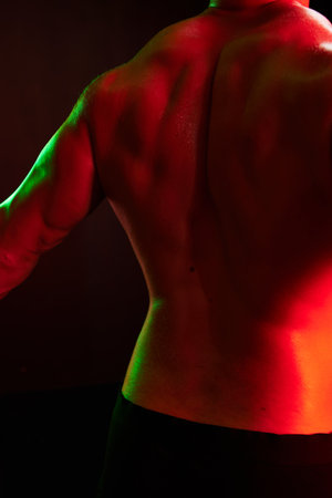 Man bodybuilder athlete with naked torso in sports uniform, isolated on black background in neon light. Advertising, sports, active lifestyle, colored light, competition, challenge concept.の写真素材