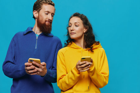 Woman and man cheerful couple with phones in their hands crooked smile cheerful, on blue background. The concept of real family relationships, talking on the phone, work online.の写真素材