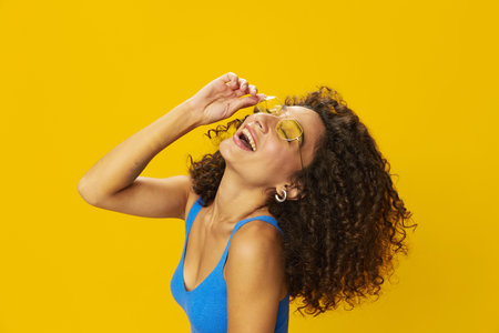 Woman with curly afro hair in a blue T-shirt on a yellow background dancing flying hair with...