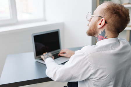 A man wheelchair businessman with tattoos office works at a laptop online, social networks and...