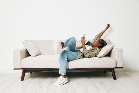 African American woman business freelancer working sitting on the couch at home in the phone, business calls and messages happiness smile, home clothes and eyeglasses, light interior background.の写真素材