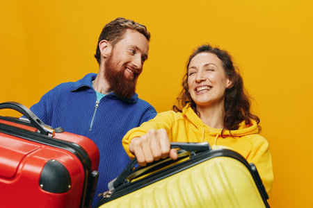 Woman and man smiling, suitcases in hand with yellow and red suitcase smiling merrily and crooked, yellow background, going on a trip, family vacation trip, newlyweds.の写真素材