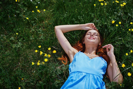 Woman smile lies on the green grass in the summer sun with yellow flowers, happiness, red long hairの写真素材