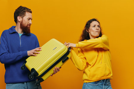 Woman and man smiling, suitcases in hand with yellow and red suitcase smiling merrily and crooked, yellow background, going on a trip, family vacation trip, newlyweds.の写真素材