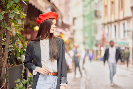 Woman smile fashion model walks on the street in the city center among the crowd in a jacket and red beret and jeans, cinematic french fashion style clothing, travel to istanbulの写真素材