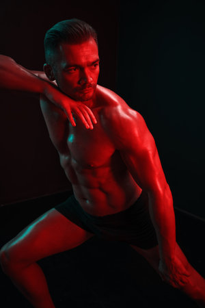 Man bodybuilder posing muscles with nude fitness torso, isolated on black background in neon light. Advertising, sports, active lifestyle, colored light, competition, challenge concept.の写真素材