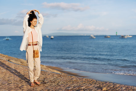 A woman happy with her eyes closed in the sun walking on the beach with her arms spread out against the ocean with a smile, flying hair, tanned skin, relaxation, a trip to the ocean and freedom.の写真素材