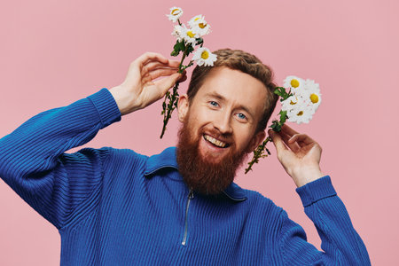 Portrait of a funny man smiling with a bouquet of flowers daisies on pink isolated background, copy place. Holiday concept and congratulations, Valentines Day, Womens Day.の写真素材