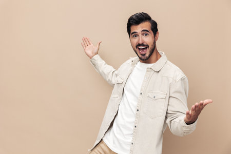 Portrait of a stylish man smile with teeth and surprise raised his hands up on a beige background in a white t-shirt, fashionable clothing style, copy space, space for textの写真素材