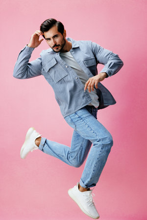 Man with beard jumping on pink background in white T-shirt and jeans, smile and joyful emotion on his face, full-length, copy spaceの写真素材