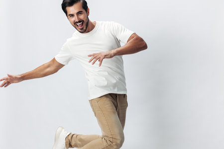 Fashion man jumping and running in a white t-shirt and jeans, smile with teeth joy on a white isolated background, fashionable clothing style, copy space, space for textの写真素材