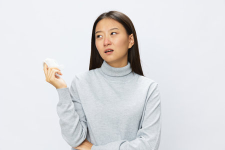 Sad Asian woman holding hand with handkerchief and coughing up flu and cold, stuffy nose viral disease asthma and allergies covid, white backgroundの写真素材