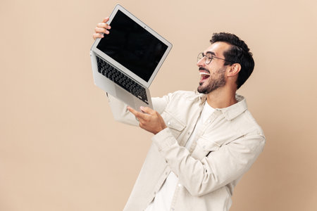 Portrait of a stylish with a laptop in his hands mockup, working freelancer smile with teeth open mouth, on a beige background in a white t-shirt, fashionable clothing style, space spaceの写真素材