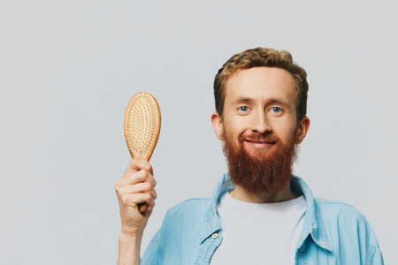 Portrait of a man with a massage comb in his hands, combing his hair and beard, hair loss problemの写真素材