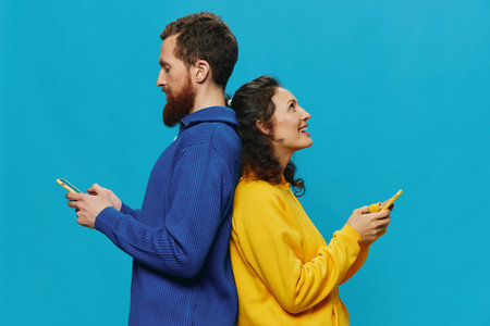 Woman and man cheerful couple with phones in their hands crooked smile cheerful, on blue background. The concept of real family relationships, talking on the phone, work online.の写真素材