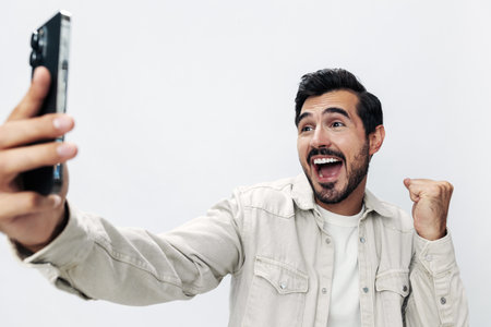 Close-up portrait man with a phone in his hands makes a selfie blogger smile open mouth surprise on a white isolated background, fashionable clothing style, copy space, space for textの写真素材