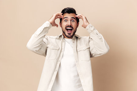 Portrait of a stylish man smile with teeth happiness opened his mouth in surprise on a beige background in a white t-shirt looks at the camera, fashionable clothing style, copy space, space for textの写真素材